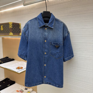 A premium Prada Logo Short-Sleeve Denim Shirt hanging on display, showcasing a faded blue wash and an enameled metal logo pocket.
