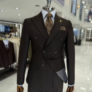Mannequin showcasing a men's dark brown pinstripe double-breasted suit with an asymmetric wrap detail, a brown textured tie, and a white shirt.