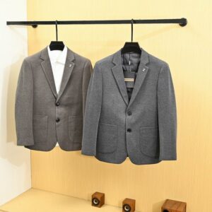 Two men's premium knit blazer jackets in grey and olive brown hanging on a black clothes rack next to a white bookshelf.