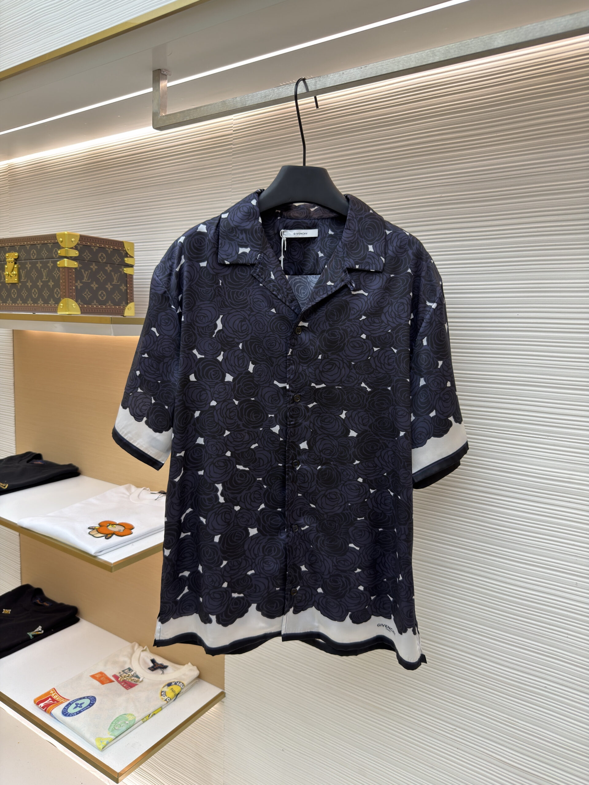 Front view of a Givenchy Midnight Rose Print Silk Short-Sleeve Shirt hanging in a luxury boutique, featuring a black rose pattern and white border.
